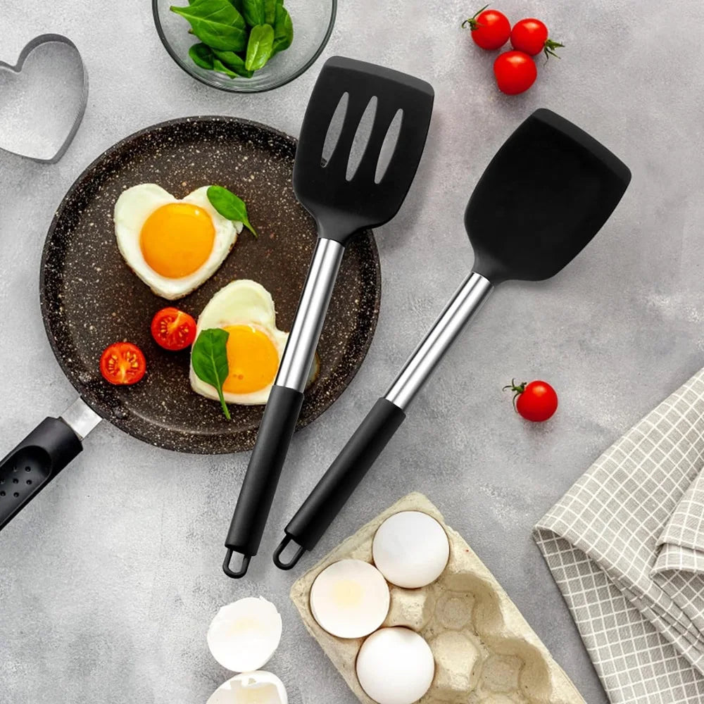 Spatules silicone inox haute résistance – Set 2 spatules , présentation sur une table des 2 spatules en silicone posés à coté d'une poêle remplie de deux oeufs aux plats