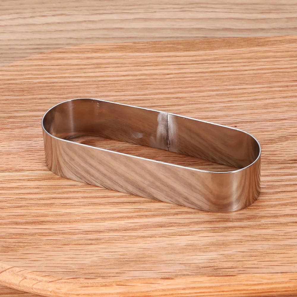 Moule à Gâteau et Tartelette Inox – Durable & Éco. Emporte-pièce ovale en acier inoxydable posé sur planche en bois