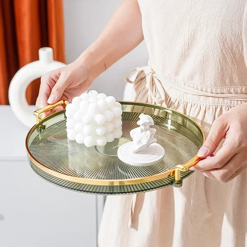 Mains tenant un Plateau Rond Acrylique avec Poignées Dorées – Déco & Service affichant bougie bulle blanche et figurine décorative