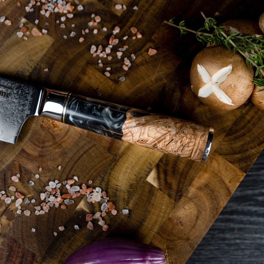 Poignée en bois et acier d'un Couteau de Chef Baovim 20,5 cm posé sur une planche en bois avec herbes et champignons