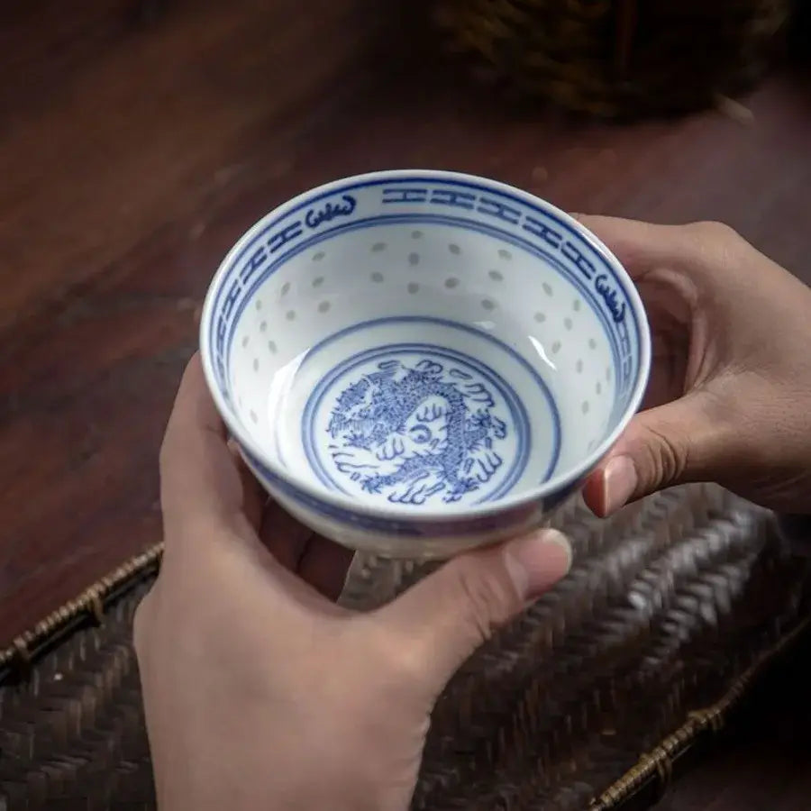 Bol en Porcelaine Chinoise avec motifs traditionnels, tenu à deux mains sur table en bois