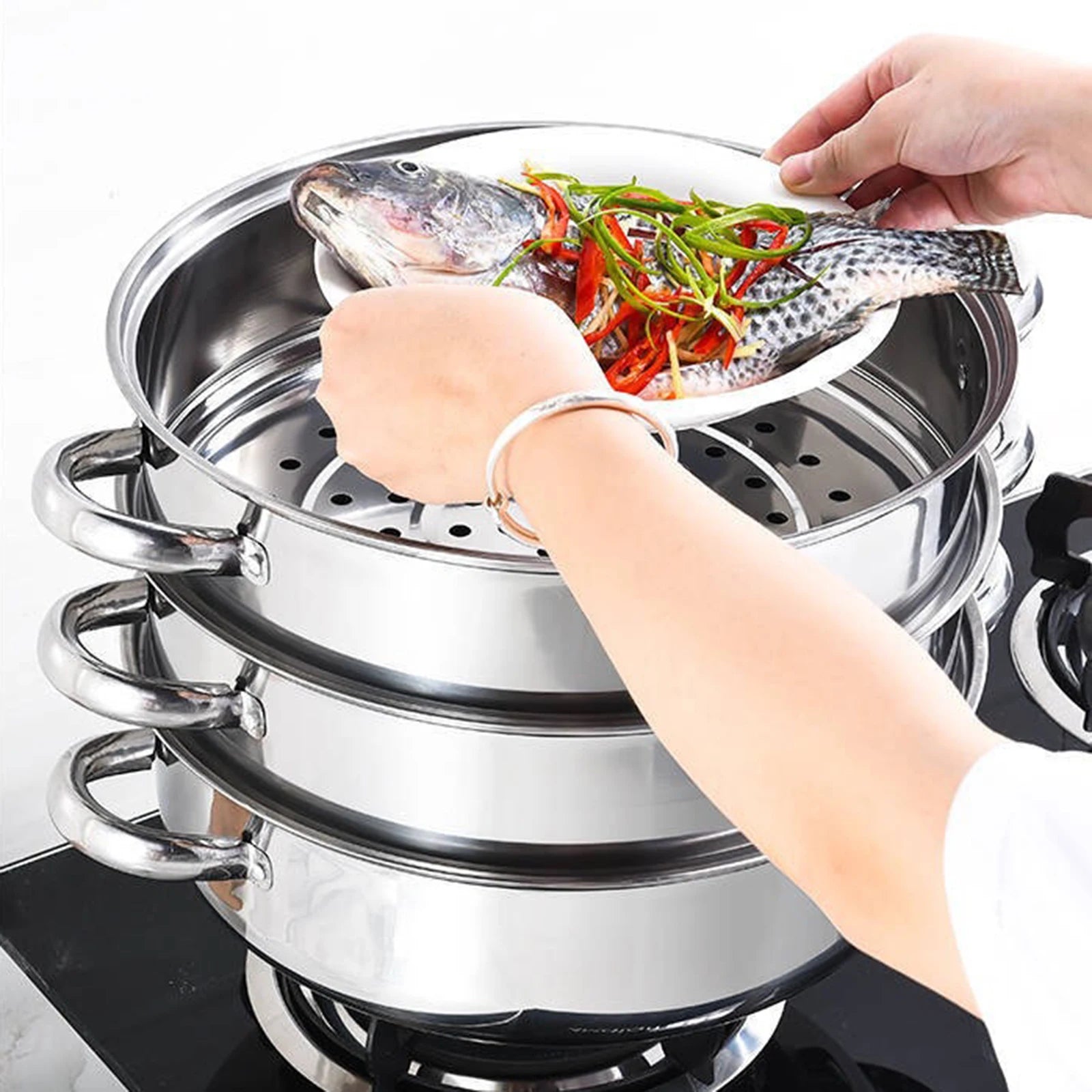 Cuit vapeur inox 3 niveaux – Cuisson saine rapide. Mains déposant un poisson garni dans le panier vapeur en inox