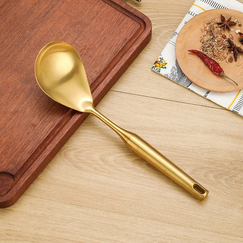Cuillère dorée de cuisine en couverts en acier inoxydable doré posée sur planche en bois