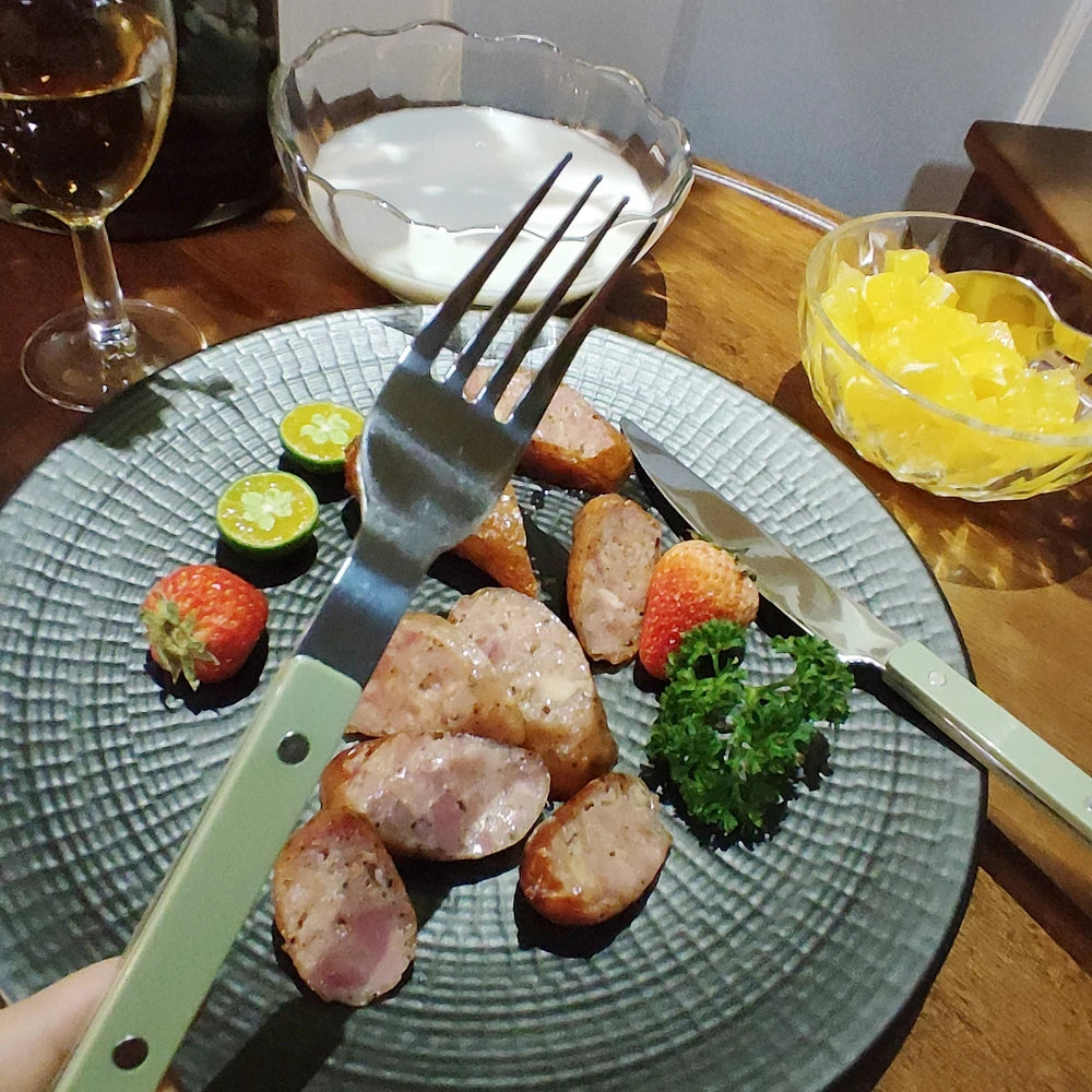 Couverts Inox 18/10 Premium Kit Complet 4 Pièces avec une assiette garnie de saucisses et de fruits