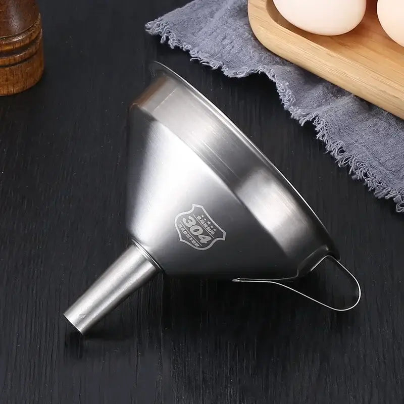 Entonnoir de Cuisine Inox 304 Précis et Durable posé sur une table avec des œufs et un linge de cuisine