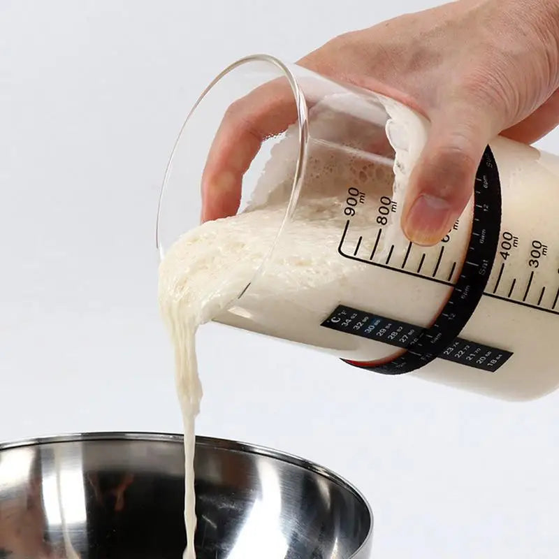 Main versant un levain dans un bol en inox avec Kit Fermentation Maison – Pot Levain