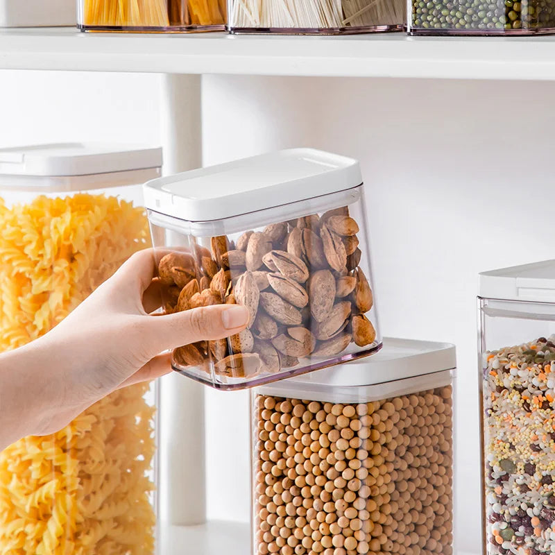 Main saisissant une boîte remplie d'amandes parmi des Boîtes de Conservation Transparentes Hermétiques – METKA sur étagère de cuisine