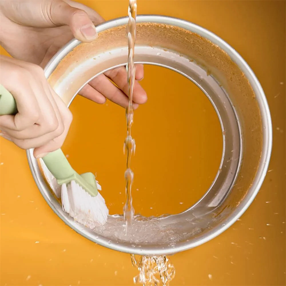 Moule à gâteau rond en aluminium fond amovible en cours de nettoyage sous un jet d'eau avec une brosse