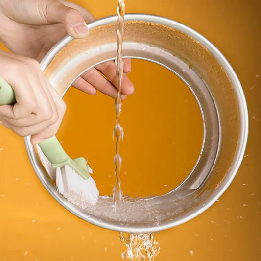 Moule à gâteau rond en aluminium fond amovible en cours de nettoyage sous un jet d'eau avec une brosse