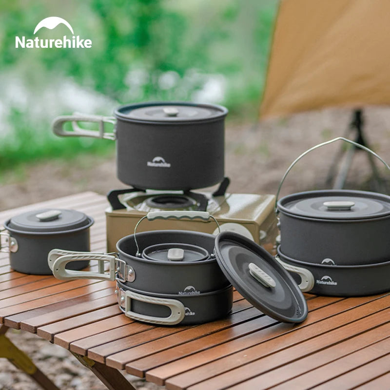 Batterie de Cuisine Camping Naturehike noire avec casseroles et poêles sur une table en bois en extérieur