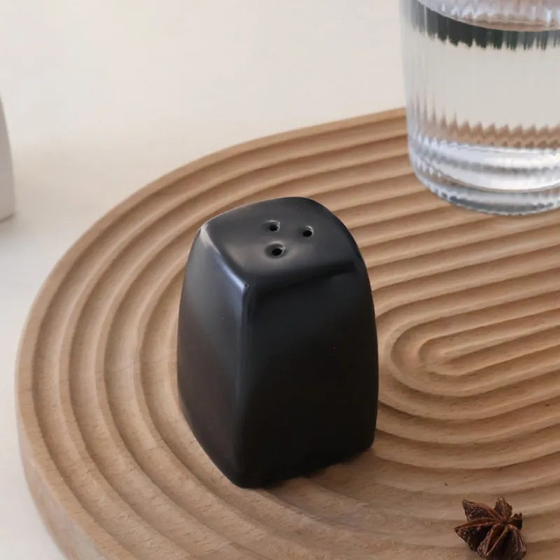 Salière et Poivrière en Céramique – Duo Fait Main Design noir posé sur un plateau en bois avec verre d'eau