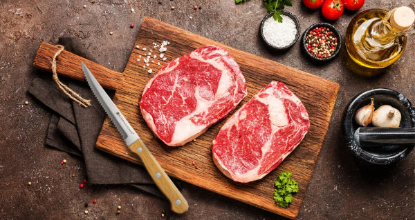 Set 4 à 8 Couteaux à Steak Dentelés – Manche Bois Naturel posé à côté de deux steaks crus sur une planche en bois