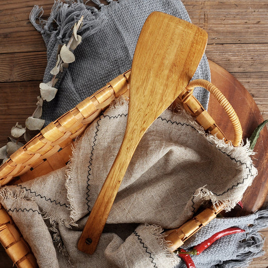 Spatule en Bois Naturel pour Poêle Antiadhésive placée dans un panier en osier sur un tissu doux