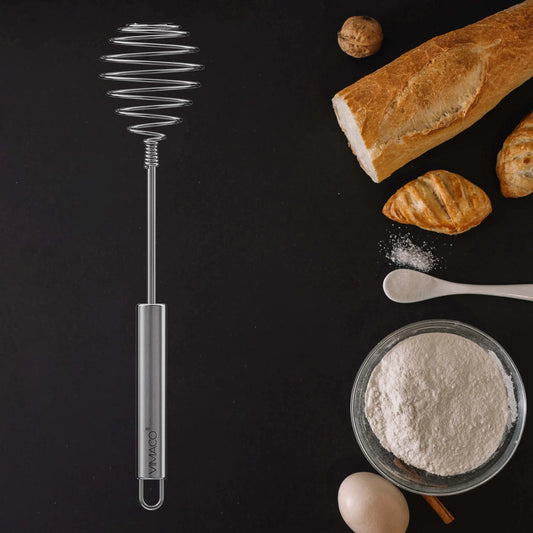 Fouet à œufs manuel inox en acier inoxydable posé sur fond noir avec farine œuf et baguette