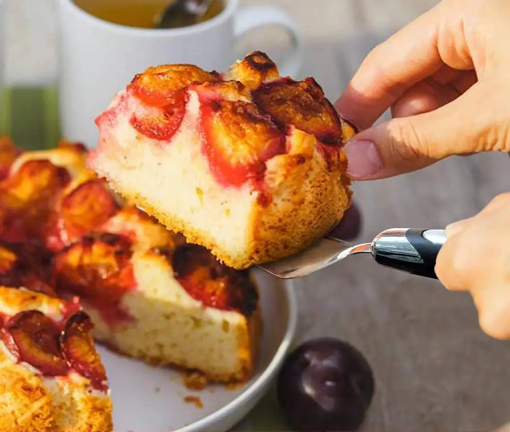 Spatules Inox Pâtisserie – Découpe Gâteaux & Tartes, main soulevant une part de gâteau aux prunes sur une spatule inox