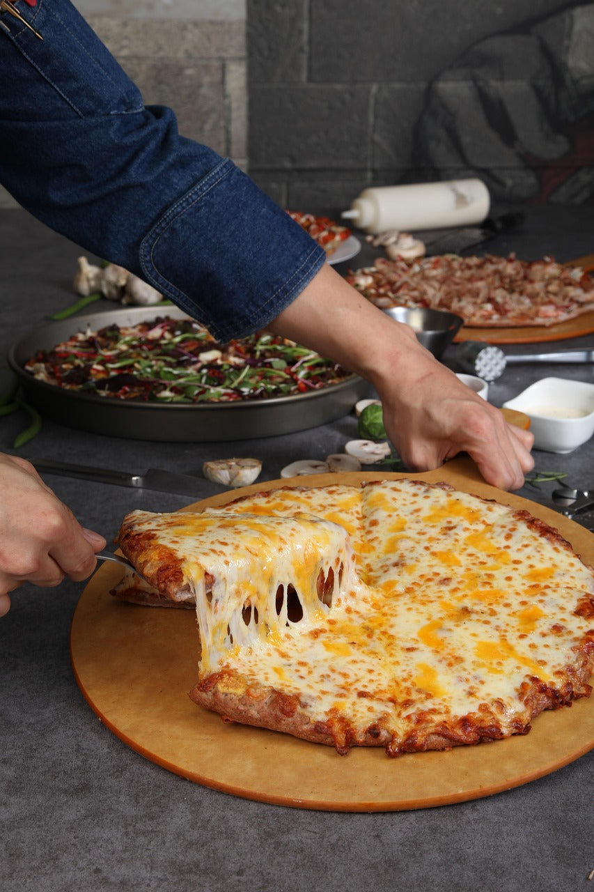 Recettes de pizza maison : Histoire, Cuisson et idées. Personne coupe une pizza au fromage fondant sur une planche en bois