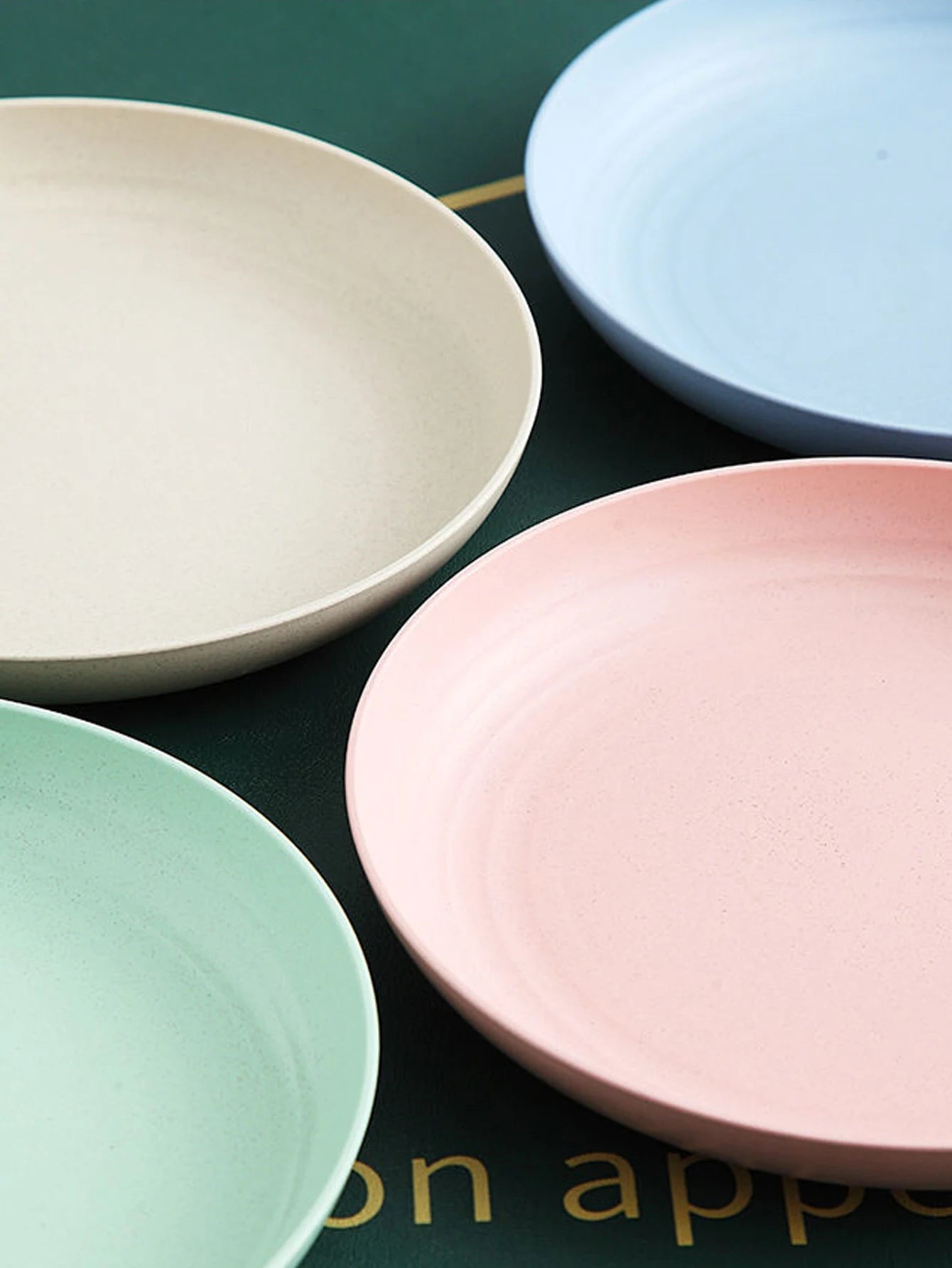 Assiettes rondes incassables en paille de blé dans des couleurs pastel sur une surface verte