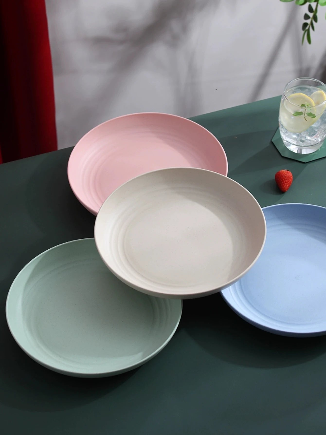 Assiettes rondes incassables en paille de blé de couleurs pastel sur une table avec un verre de limonade