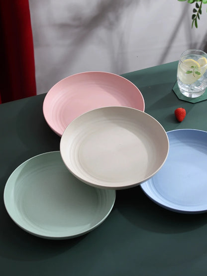 Assiettes rondes incassables en paille de blé de couleurs pastel sur une table avec un verre de limonade