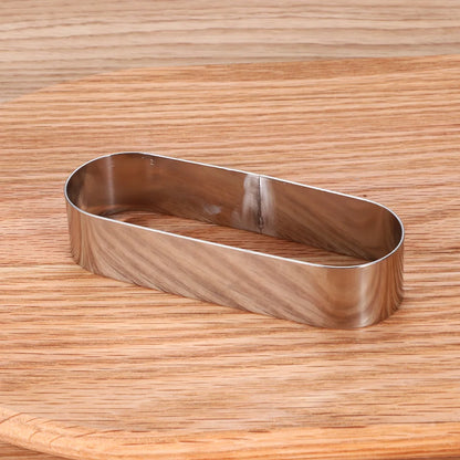 Moule à Gâteau et Tartelette Inox – Durable & Éco. Emporte-pièce ovale en acier inoxydable posé sur planche en bois