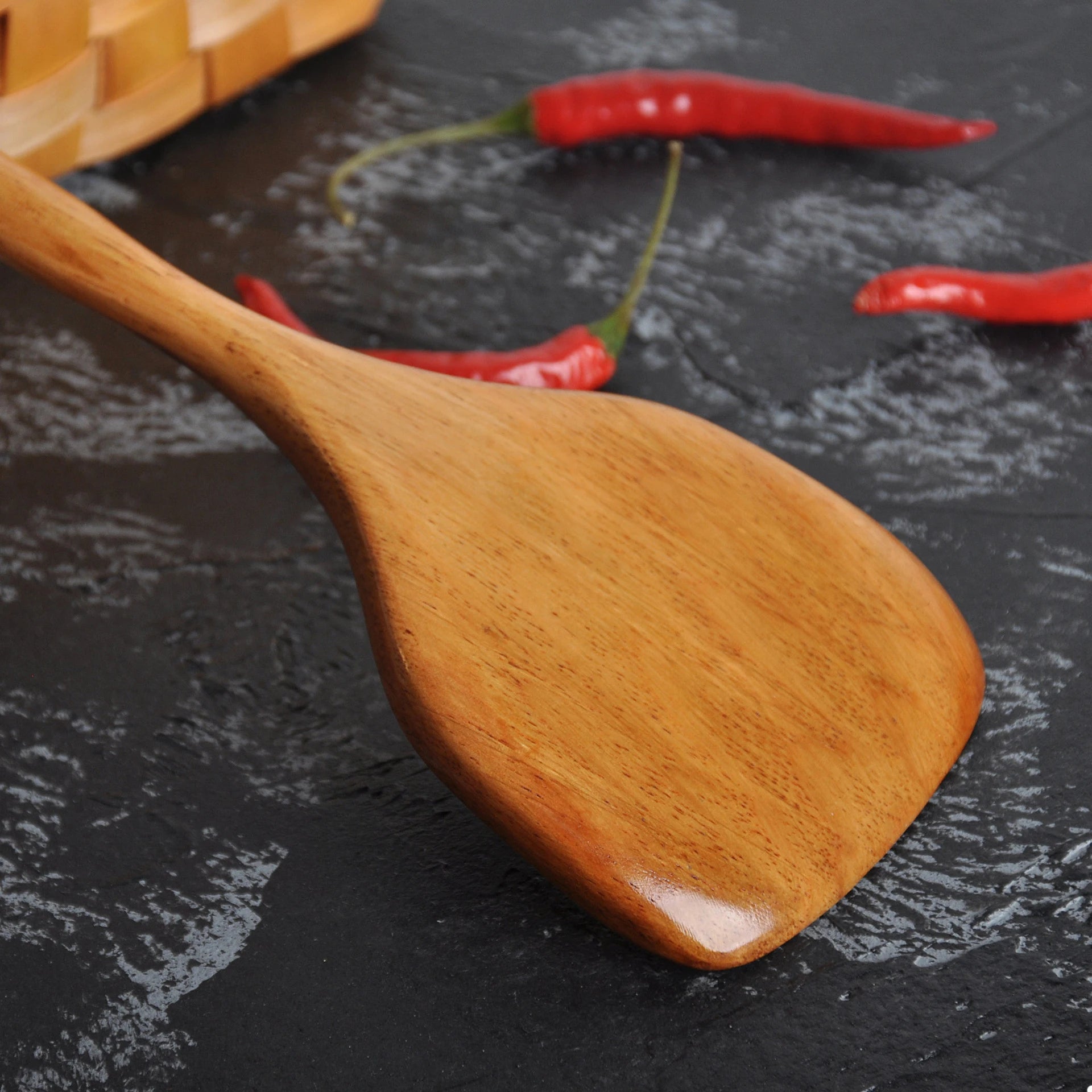 Spatule en Bois Long Manche – Ustensile de Cuisine Durable en bois verni manche long posée sur plan sombre avec piments
