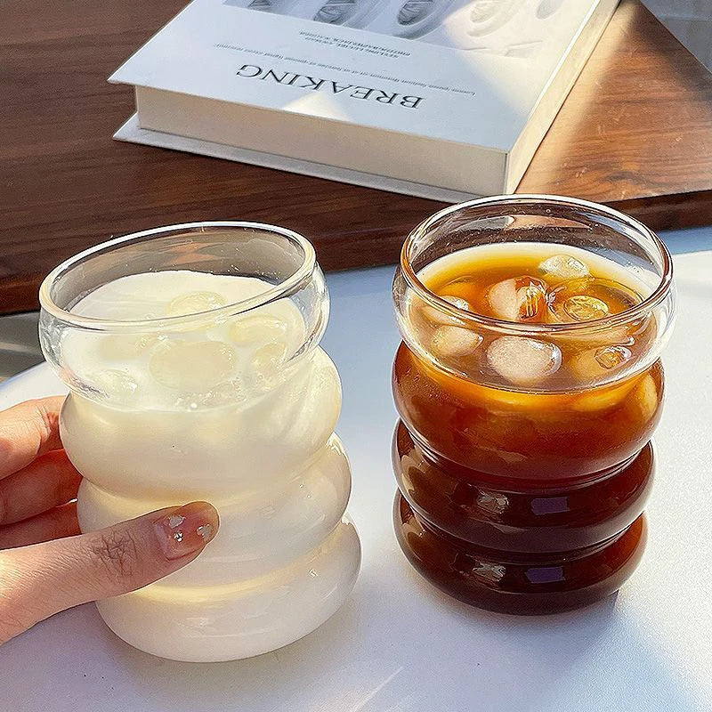 Verre Tumbler Ondulé Transparent – Élégant & Pratique. Deux verres ondulés, lait et café glacé, glaçons, main tenant un verre
