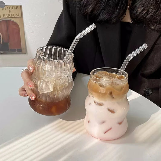 Verre Tumbler Ondulé Transparent – Élégant & Pratique. Deux verres ondulés avec glaçons et pailles en verre, tenu à la main