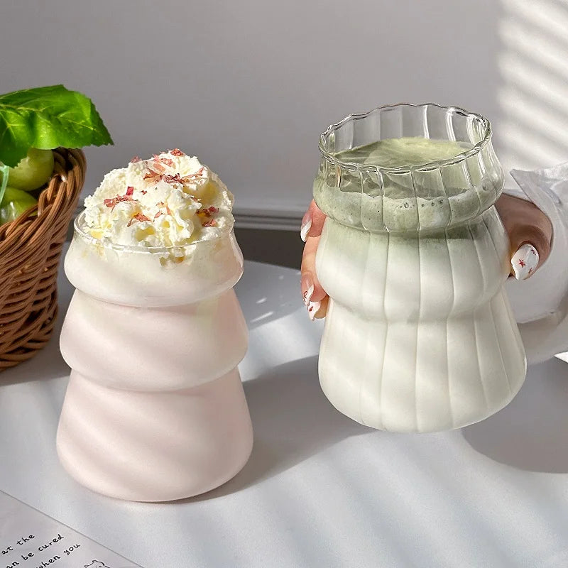 Verre Tumbler Ondulé Transparent – Élégant & Pratique. Verre transparent avec latte matcha tenu à côté d'un rose crème