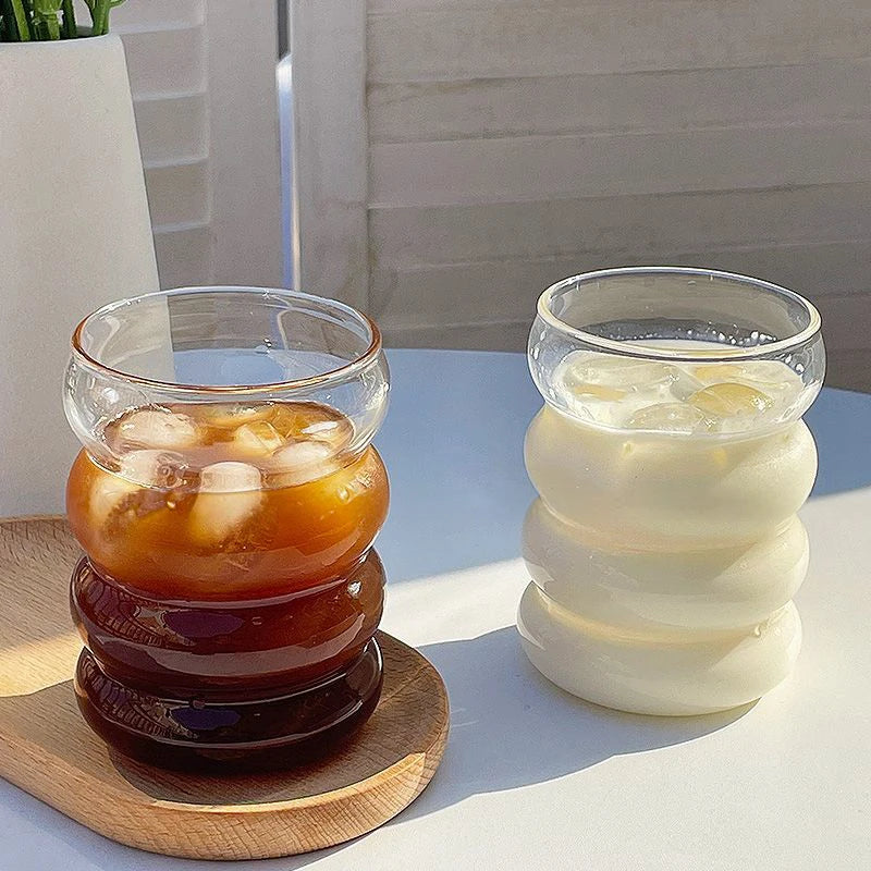 Verre Tumbler Ondulé Transparent – Élégant & Pratique. Deux verres ondulés transparents, café glacé et lait frais sur table.