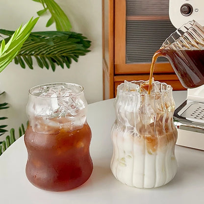 Verre Tumbler Ondulé Transparent – Élégant & Pratique. Deux gobelets ondulés, café glacé et latte versé sur table