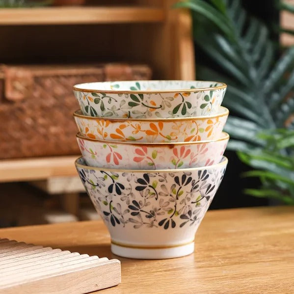 Bol en Porcelaine à Motifs Floraux - Lot de 4 empilés sur une table en bois avec des plantes en arrière-plan