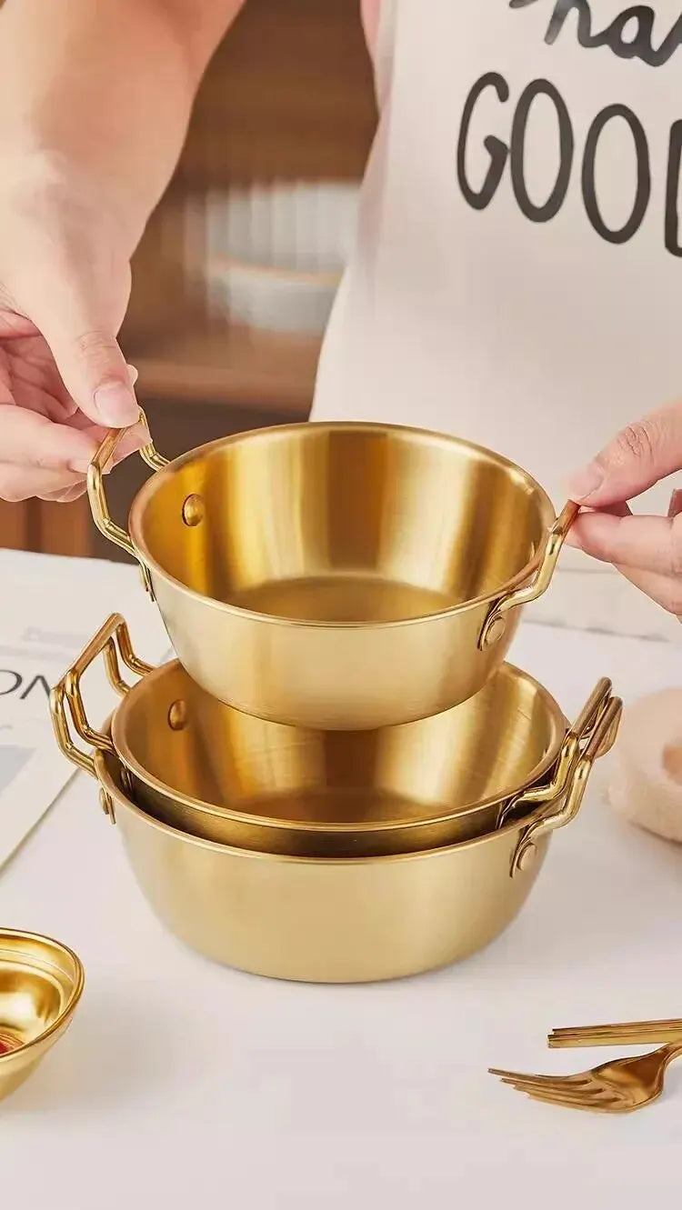 Bol Inox Doré avec Anse Anti brûlure – 12 à 14 cm tenu par des mains sur une table blanche