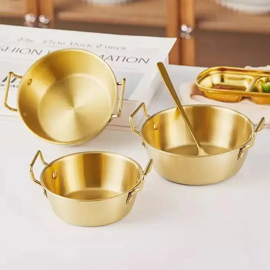 Bol Inox Doré avec Anse Anti brûlure – 12 à 14 cm disposés sur une table avec une cuillère dorée
