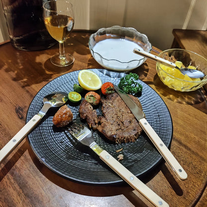 Couverts Inox 18/10 Premium Kit Complet 4 Pièces sur une table avec un plat de viande et des garnitures