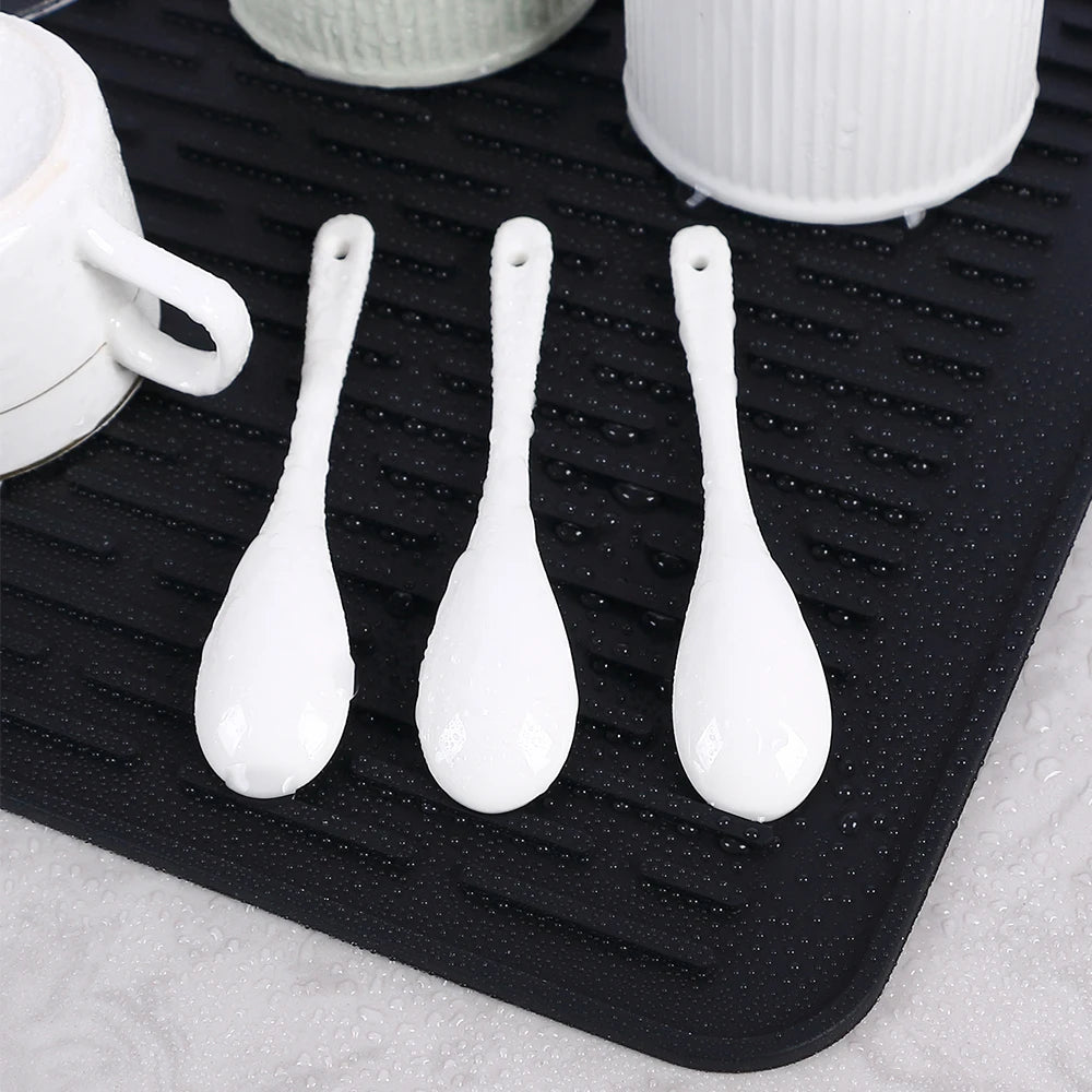 Tapis Égouttoir Silicone Multifonction noir avec tasses et cuillères blanches posées et gouttes d eau