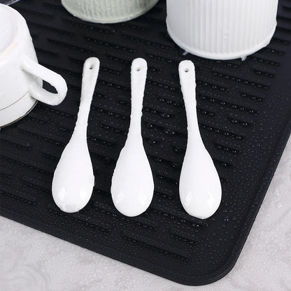Tapis Égouttoir Silicone Multifonction noir avec tasses et cuillères blanches posées et gouttes d eau