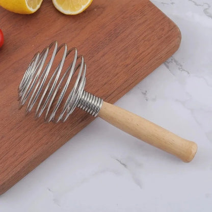 Fouet à Ressort en Inox avec Manche en Bois sur une planche à découper, idéal pour sauces et pâtisserie