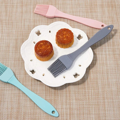 Pinceau de Cuisine en Silicone en bleu, gris et rose avec des gâteaux sur une assiette blanche
