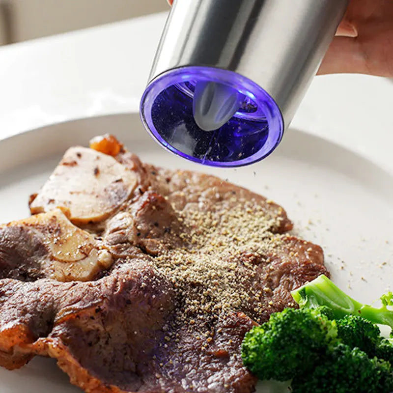 Moulin Électrique Sel & Poivre en acier inoxydable en train de moudre du poivre sur un steak avec brocoli