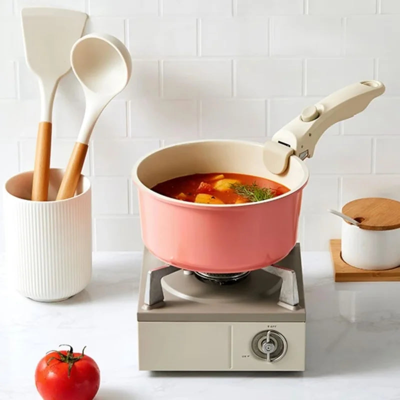 Casserole rose avec Poignée Amovible Universelle sur un réchaud, accompagnée de spatules en cuisine