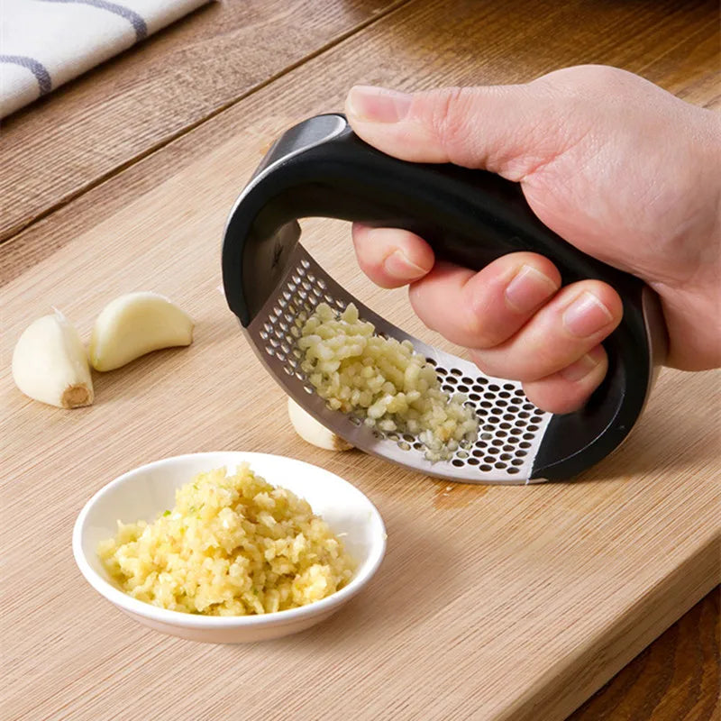 Presse-Ail Manuel Inox – Cuisine Propre, Facile & Écologique avec poignée noire et ail pressé sur planche en bois