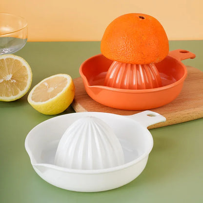 Presse-Citron Manuel Compact en Plastique – Jus Frais Maison avec deux fruits et des ustensiles de cuisine en arrière-plan.
