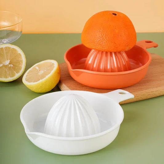 Presse-Citron Manuel Compact en Plastique – Jus Frais Maison avec deux fruits et des ustensiles de cuisine en arrière-plan.