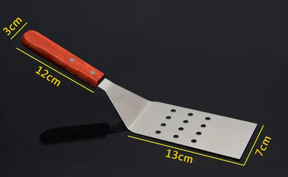 Spatule de Cuisine Inox avec manche en bois, design ergonomique et perforations pour faciliter l'évacuation des liquides.