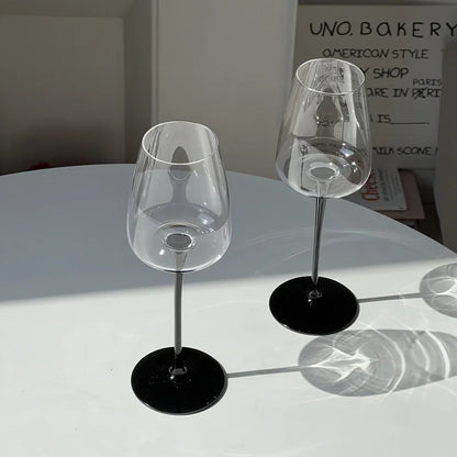 Deux verres à vin rouge Pinot Noir en cristal fin sur une table moderne avec reflets de lumière.